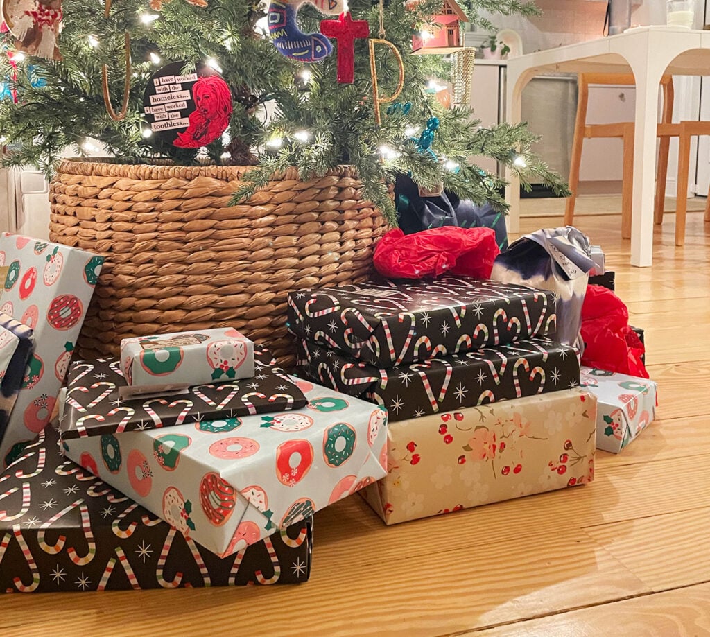 25 holiday gift exchange theme ideas 2 close up of christmas presents under a tree with woven tree skirt