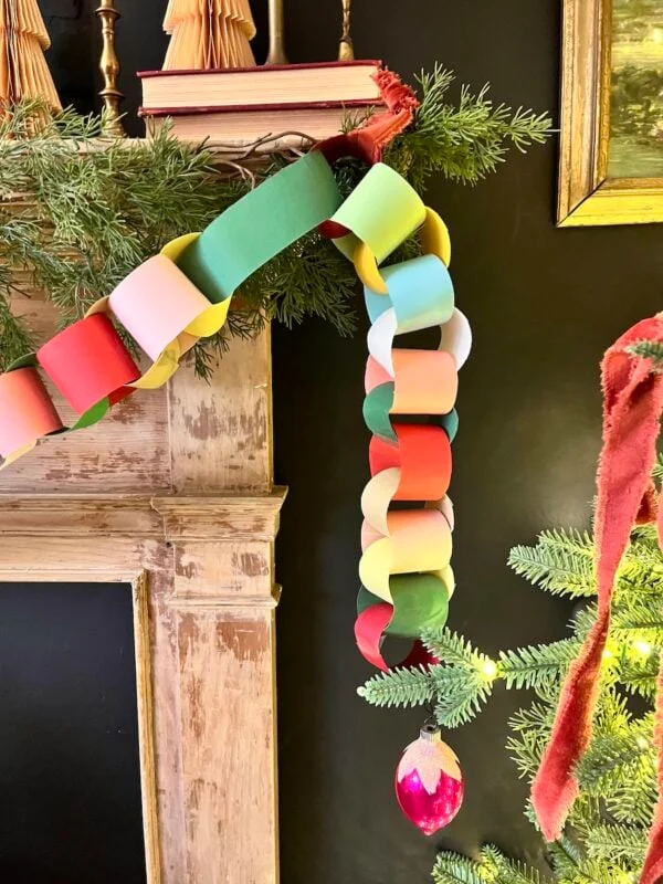 amazing and easy christmas craft paper ideas 2 a colorful paper chain garland hangs from a mantel decorated with greenery, with a red ornament attached to the end near a lit christmas tree.