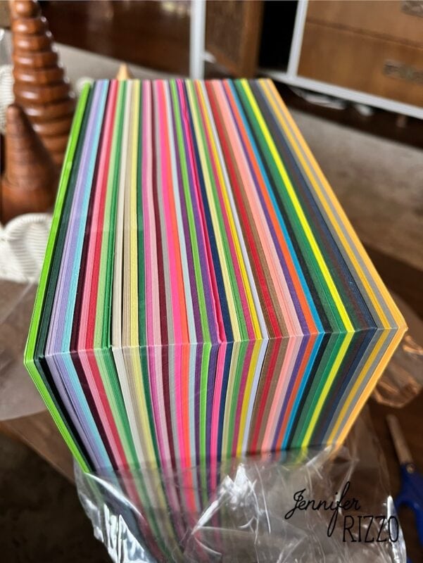 how to make an easy construction paper chain 1 a stack of multicolored paper sheets viewed from the side, showing vibrant, alternating stripes. "jennifer rizzo" is written in the bottom right corner.