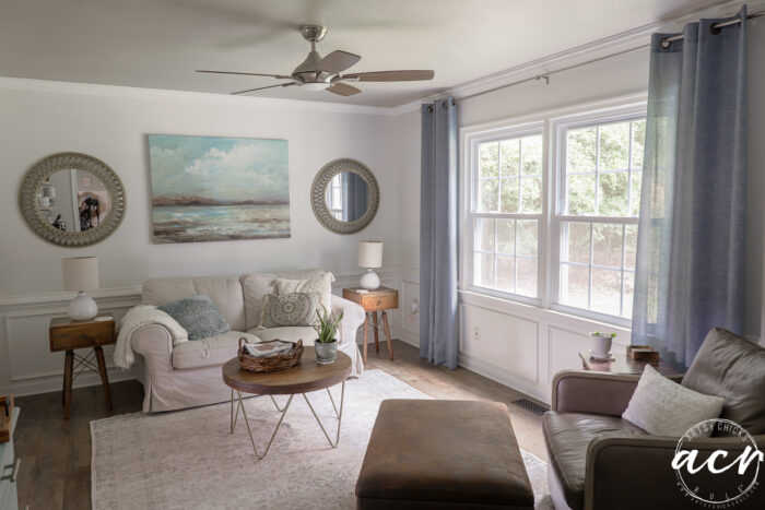 room with blue curtains, tan furniture and artwork on wall with painted ceiling