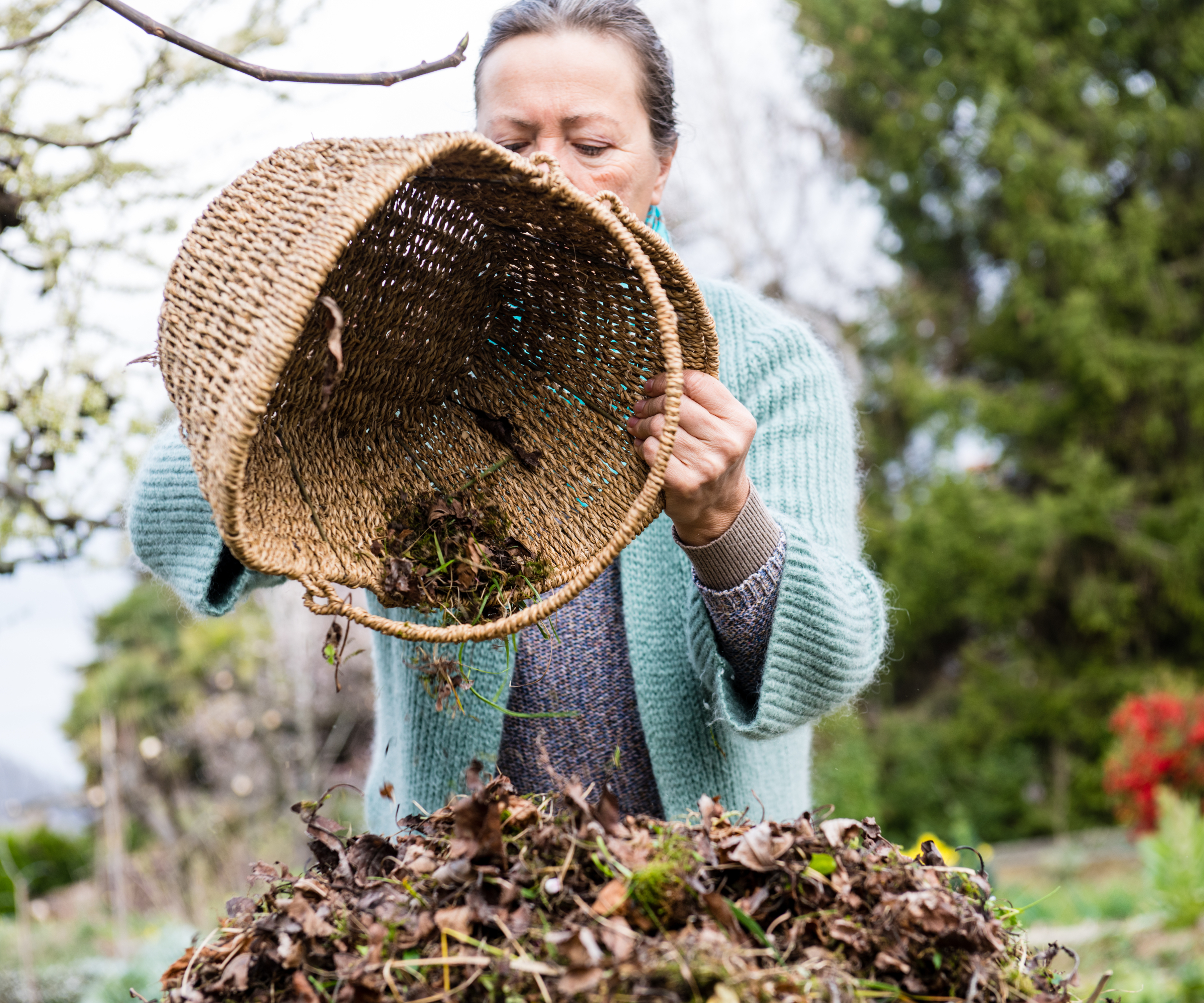 woman pours leaf litter into a compost bin from basket