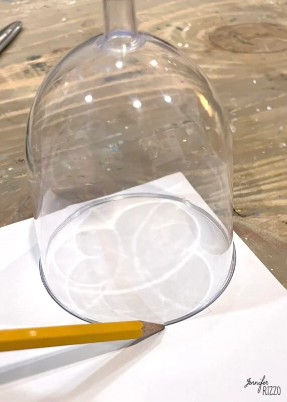 mini snow globe cloches from plastic wine glasses 2 a pencil traces the rim of an upside-down wine glass onto a sheet of white paper on a wooden surface.