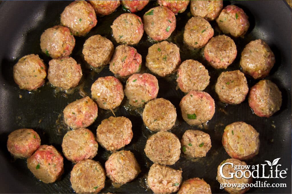 overhead view of meatballs browning in a skillet on the stovetop.