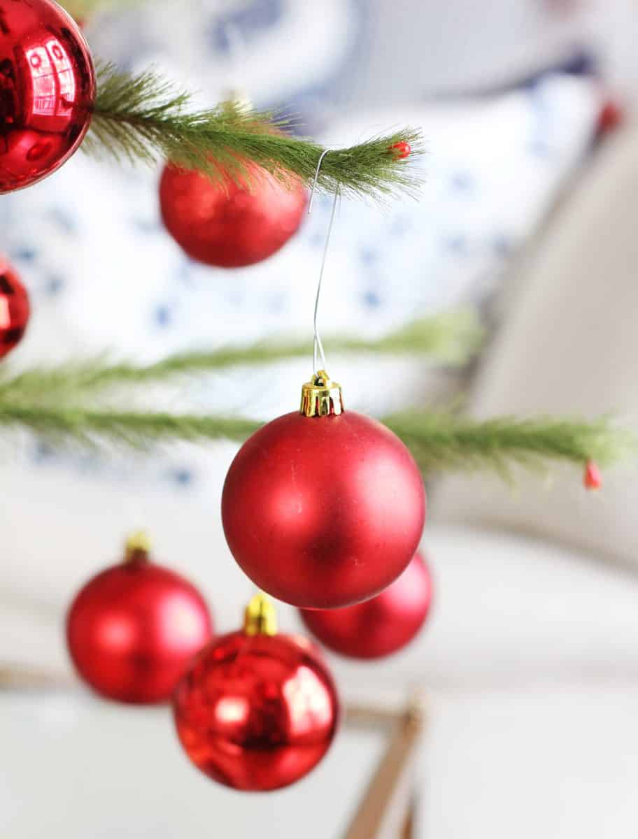 several shiny red christmas ornaments hang from the green branches of a christmas tree. the background is softly blurred with hints of neutral and blue tones.