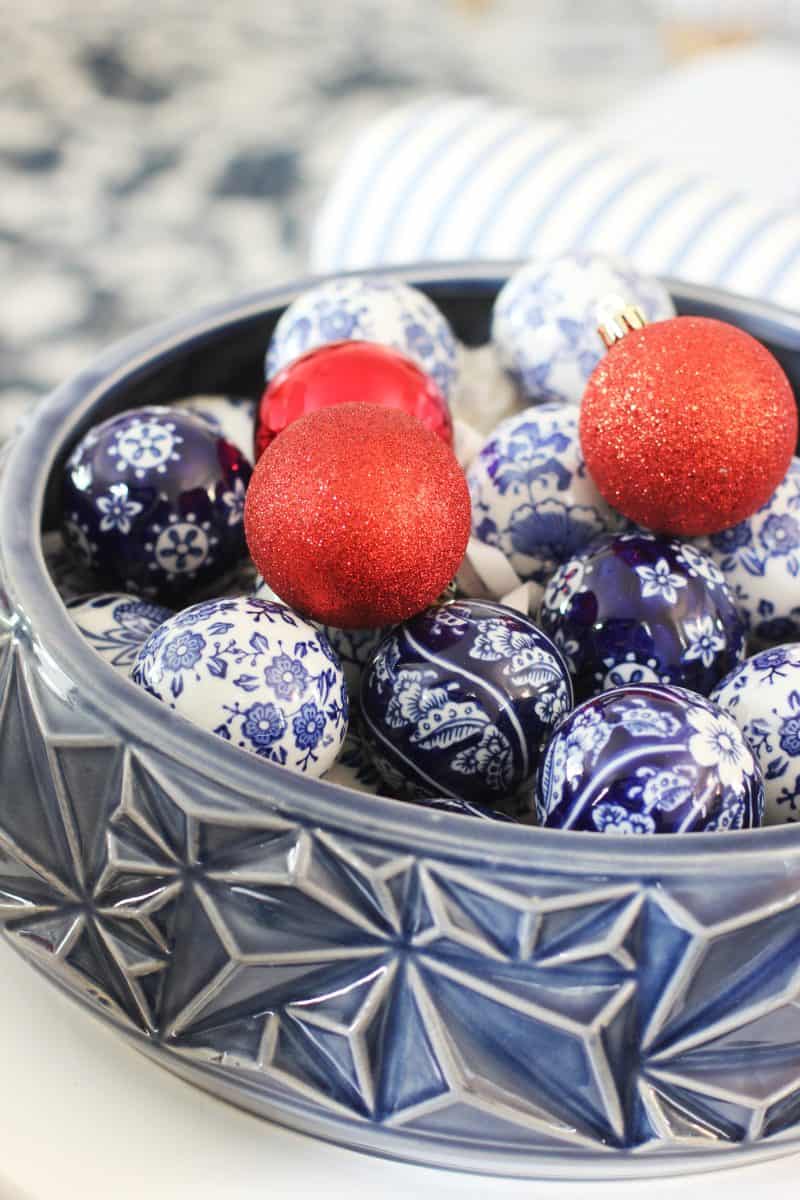 a decorative blue bowl filled with blue and white patterned ornaments and three red glittery ornaments. the bowl features a geometric star design, and the scene is bright and festive.