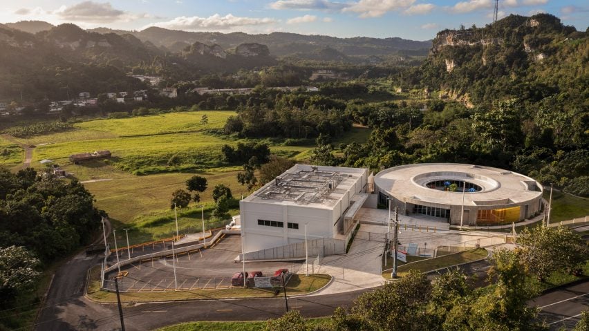 view over a ring-shaped building and a rectilinear structure, with a green valley beyond
