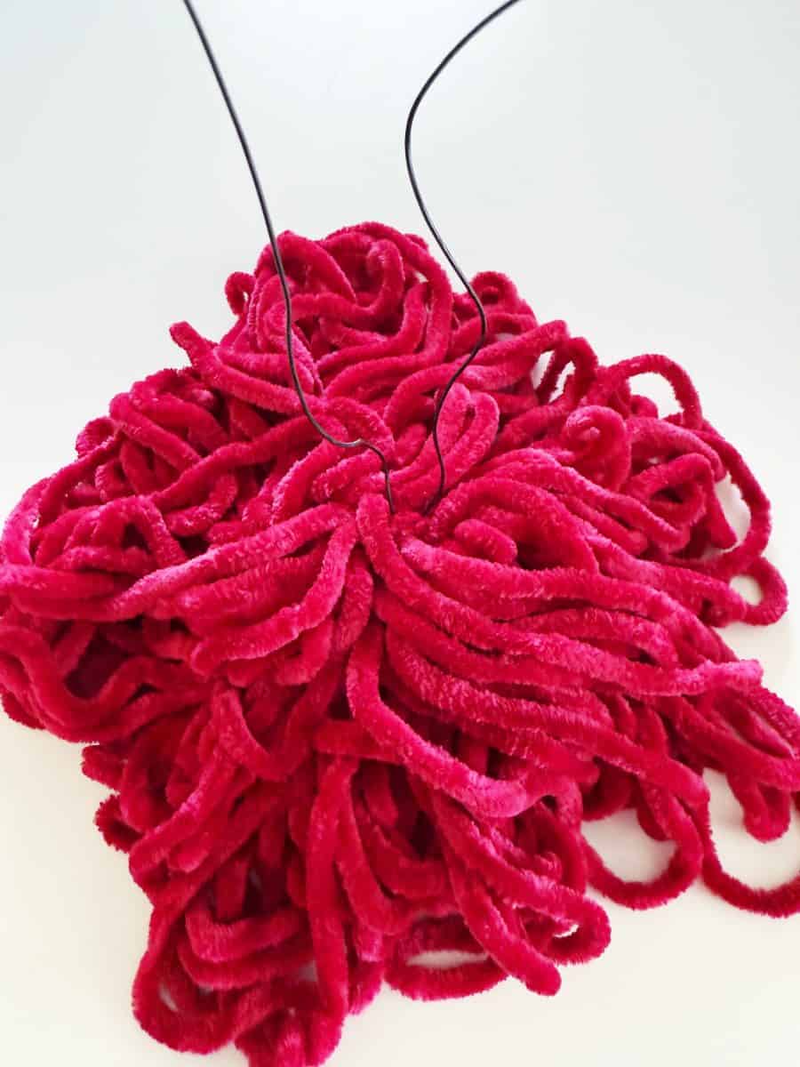 diy christmas tassel simple stepbystep tutorial 40 a cluster of bright red, plush pipe cleaners is arranged in a pile on a white surface, with two thin, black wires protruding upward from the center—perfect materials if you’re learning how to make a giant bow.
