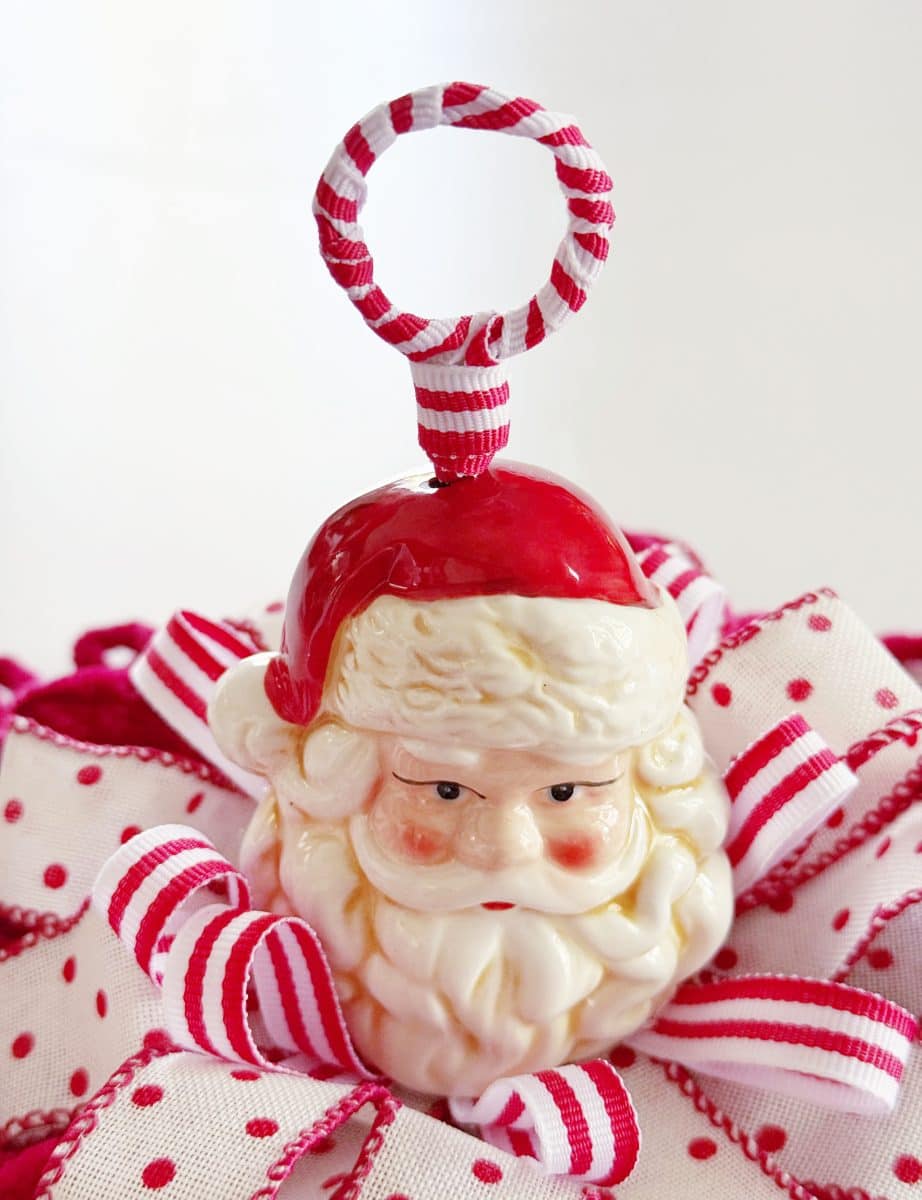 diy christmas tassel simple stepbystep tutorial 45 a ceramic santa claus ornament with a red and white striped hanging loop rests on a decorative ribbon with white and red stripes and polka dots, offering inspiration for how to make a giant bow for your next festive holiday scene.