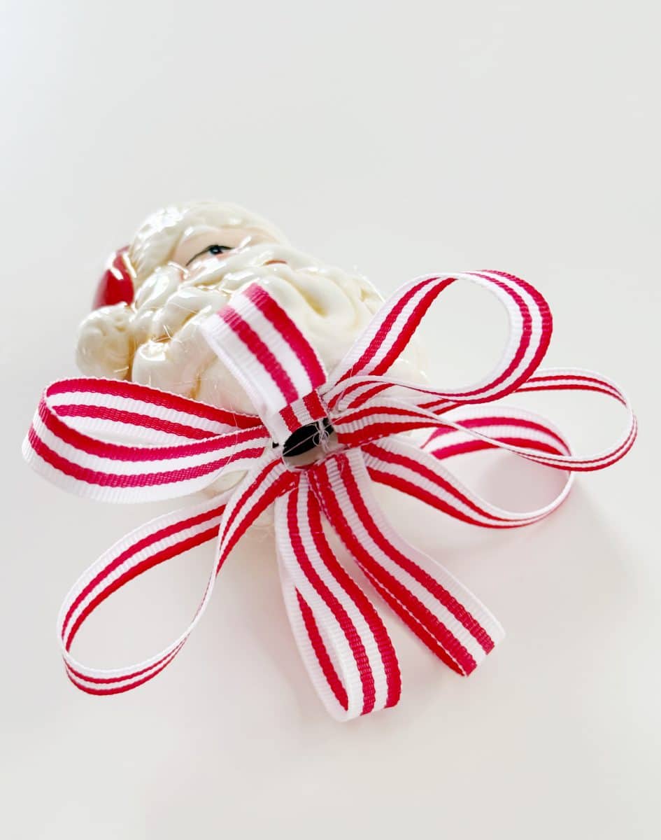 diy christmas tassel simple stepbystep tutorial 42 a red and white striped ribbon tied in a bow is attached to a white decorative object, possibly a santa claus ornament, on a plain white background—perfect inspiration if you're wondering how to make a giant bow for your holiday decor.