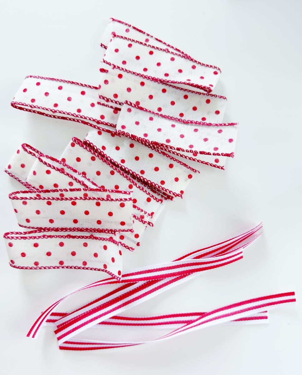 diy christmas tassel simple stepbystep tutorial 41 several pieces of white ribbon with red polka dots and red stitching are arranged on a white surface, with two striped red, white, and pink ribbons below them—perfect materials if you're wondering how to make a giant bow.