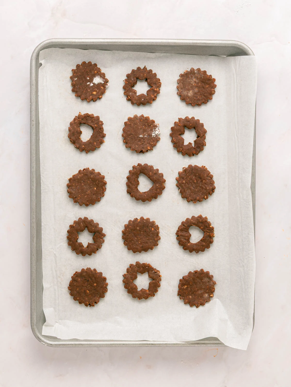 chocolate hazelnut cookies - paper and stitch 3 chocolate linzer cookies on a baking sheet, lined up and ready to bake