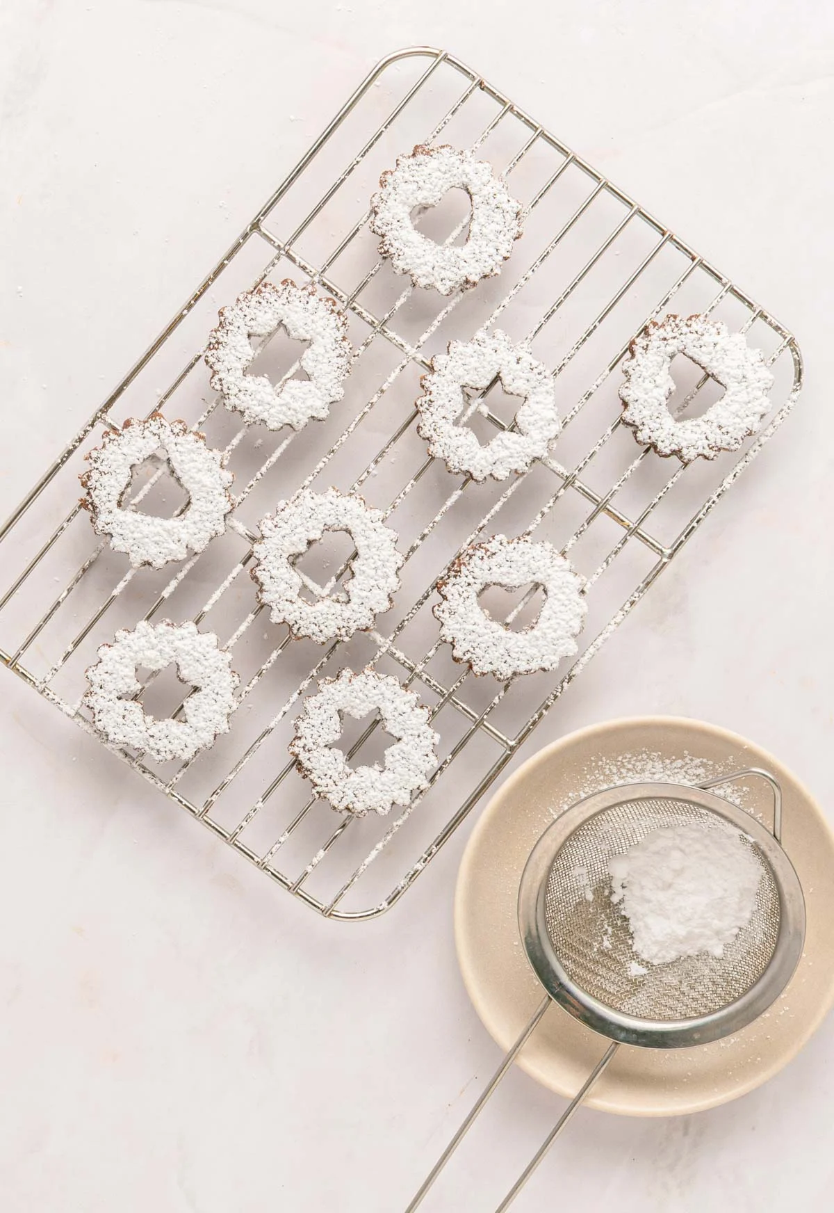 chocolate hazelnut cookies - paper and stitch 4 linzer cookies being topped with powdered sugar on a cooling rack