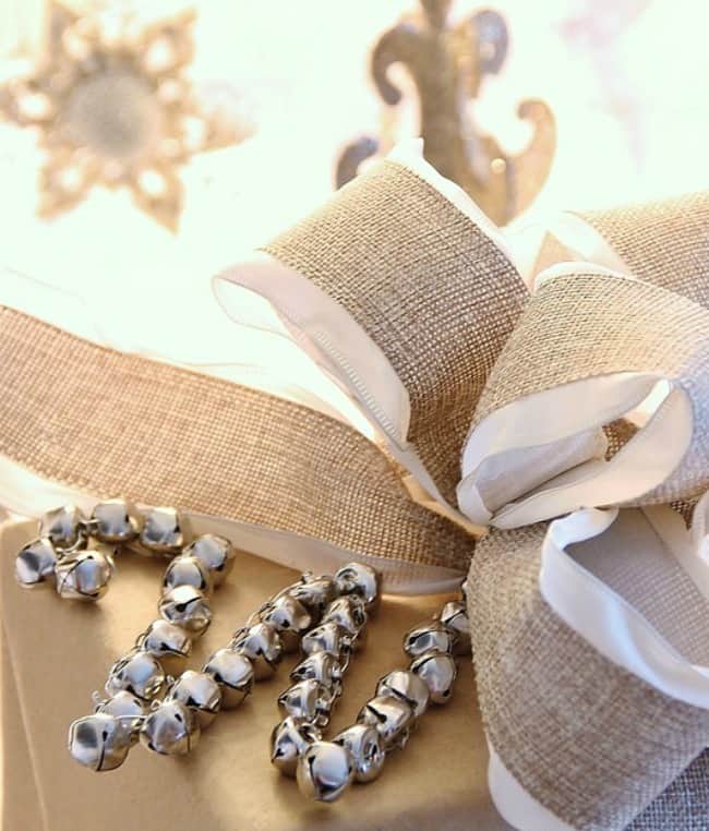 the christmas ornament that started it all 21 an elegantly wrapped gift adorned with a burlap and white satin ribbon bow, accompanied by shiny silver jingle bells that evoke a festive, holiday mood.
