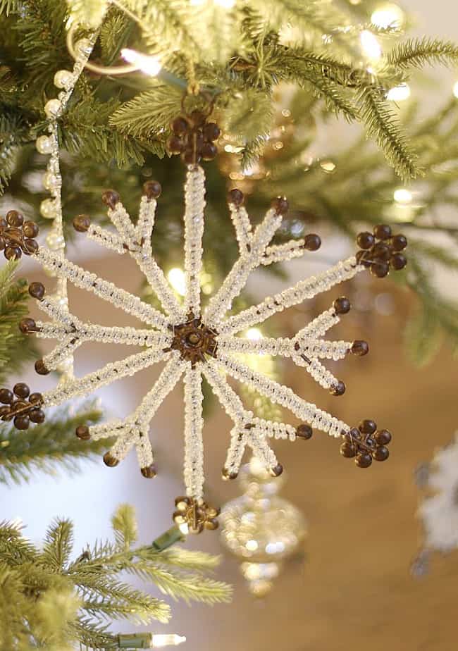 the christmas ornament that started it all 19 a sparkling white and gold beaded snowflake ornament hangs from a lush green christmas tree, surrounded by pine branches and soft-focused lights.