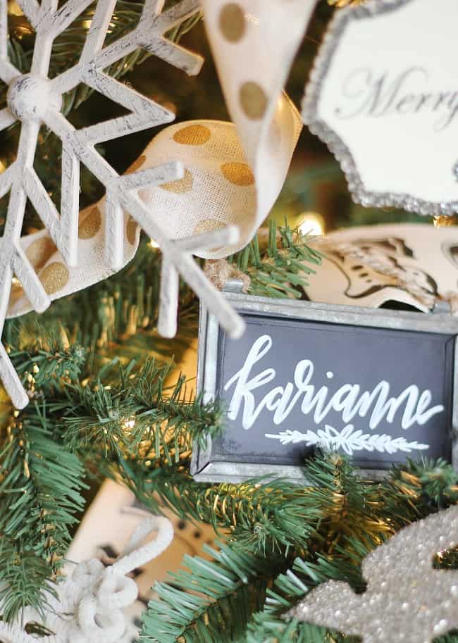 the christmas ornament that started it all 20 close-up of a christmas tree adorned with handmade ornaments and a decorative black sign that reads "karianne" in cursive white script, surrounded by white snowflakes and dotted ribbon.