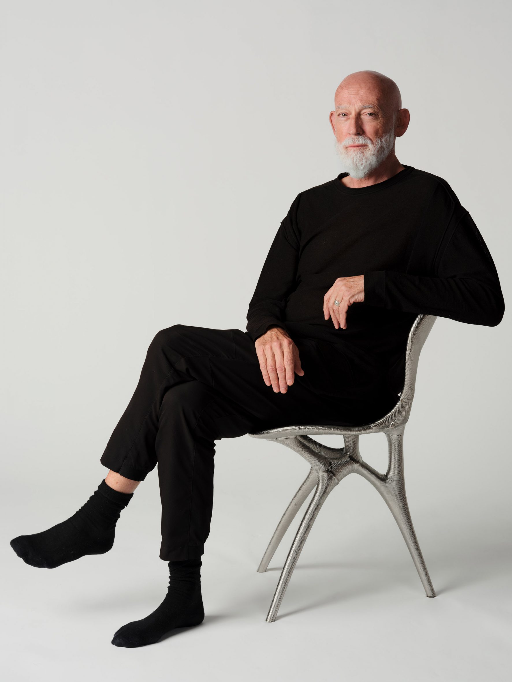 photo of ross lovegrove sitting in the metal 3d-printed chair he created with google deepmind and modem