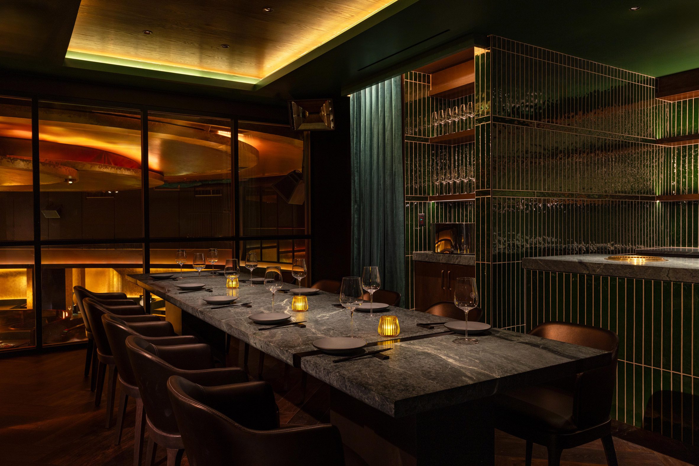 a private dining room with a long table, green-tiled walls and a window overlooking the restaurant below