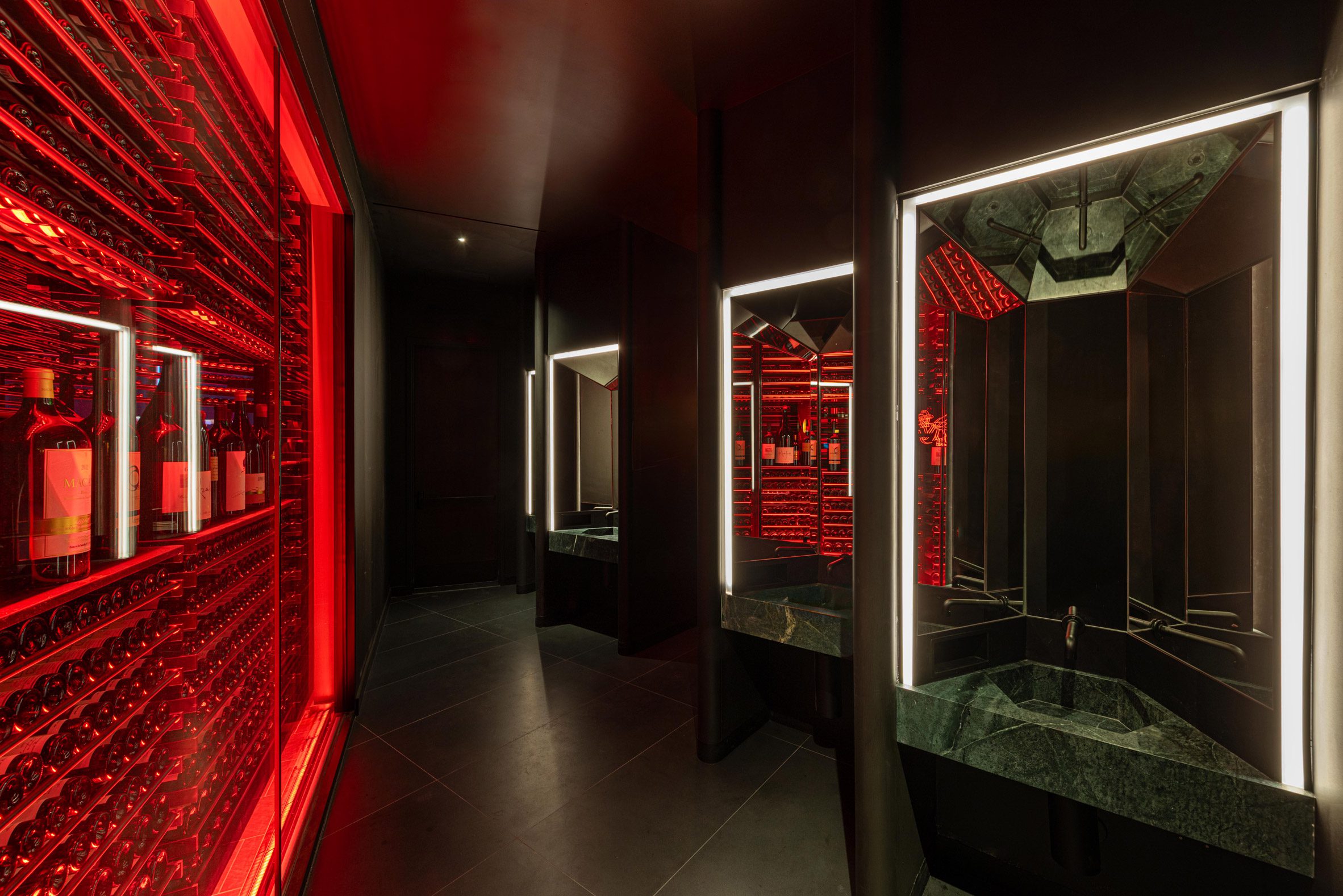 a glowing red wine rack forms a partition for a restaurant bathroom, which features green marble basins