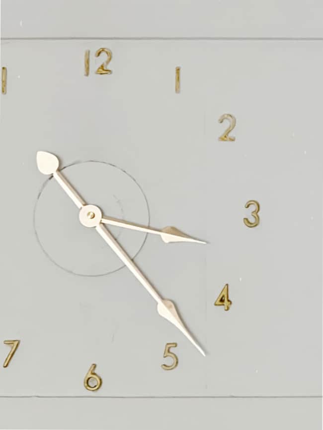 a minimalist clock face with gold numbers from 1 to 12, placed on a light gray background, showcases elegant design. the clock has two gold hands, one long and one short, indicating the current time—an inspiring example for those learning how to make a clock.