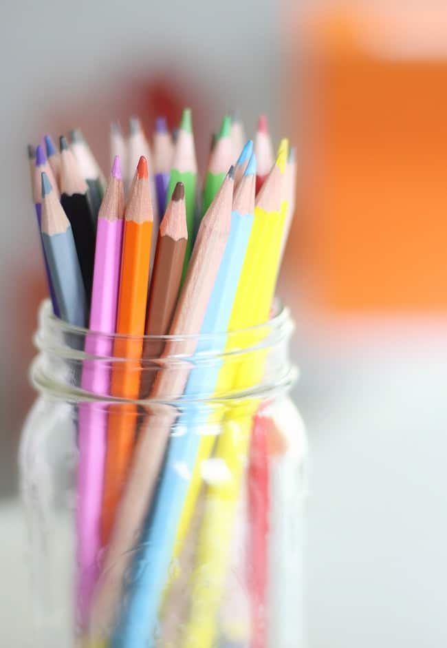a collection of sharp colored pencils in various shades, standing upright in a clear glass jar, with a softly blurred background in neutral tones, ready to bring creativity to life in the imagination room.