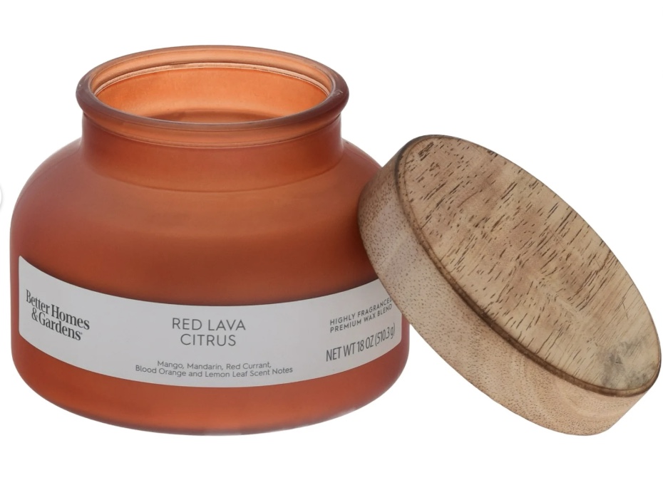 an orange glass candle jar labeled "red lava citrus" by better homes & gardens with a wooden lid resting beside it. the partially used candle reveals wax inside—perfect to make your house cozy and inviting.