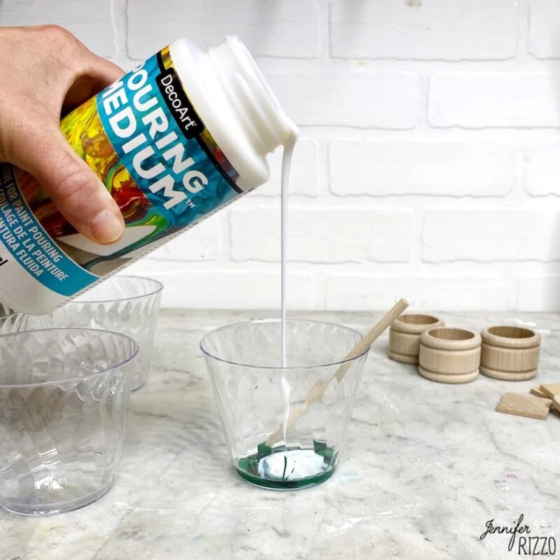 how to do acrylic paint pouring-for beginners 2 mixing decoart pouring medium with paint bring poured into in a plastic cup with green paint by a hand