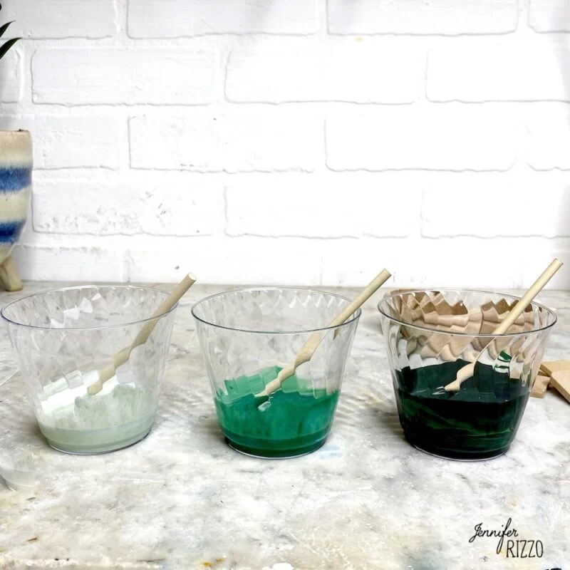 how to do acrylic paint pouring-for beginners 3 3 containers of paint in plastic cups on a table with wood sticks in them mixed with pouring medium