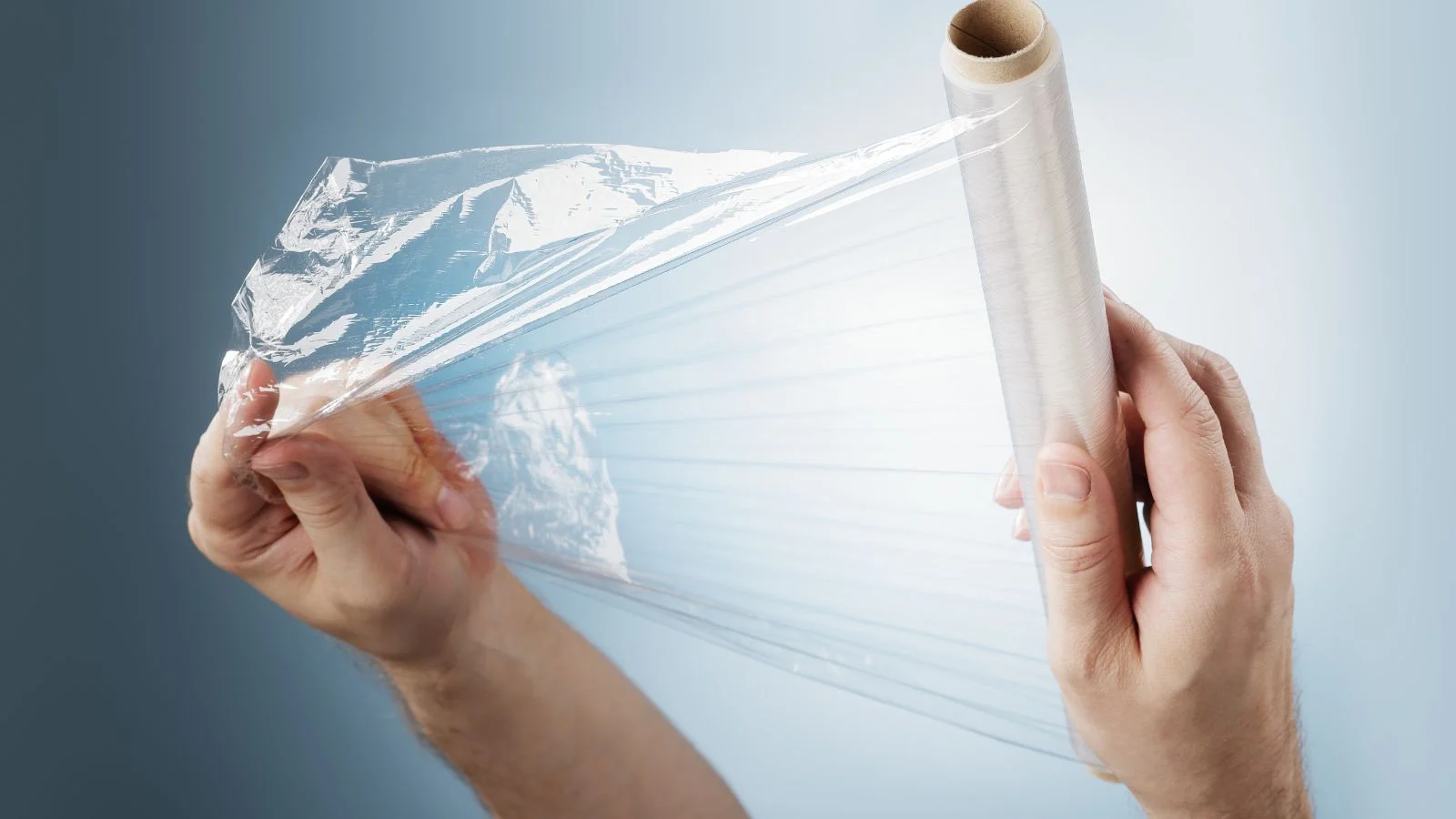 a close-up shot of a person's hands in the process of stretching out a plastic cling wrap cover, all situated in a well lit area
