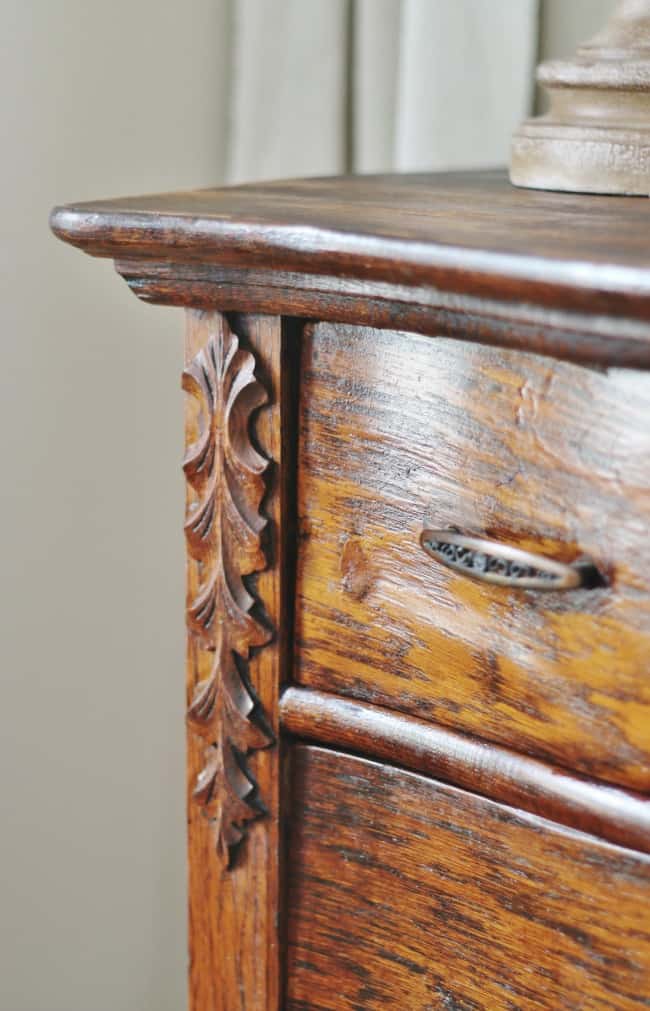 close-up of a wooden cabinet corner featuring intricate leaf carving and a vintage metal drawer handle. the wood has a rich, glossy finish.
