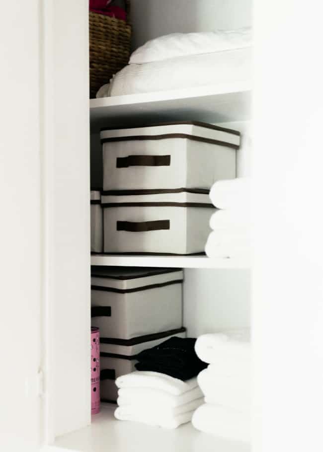 10 unexpected organizing ideas you may not have thought of 16 a neatly organized linen closet with stacked white towels, a wicker basket, and a set of three labeled storage boxes on shelves.