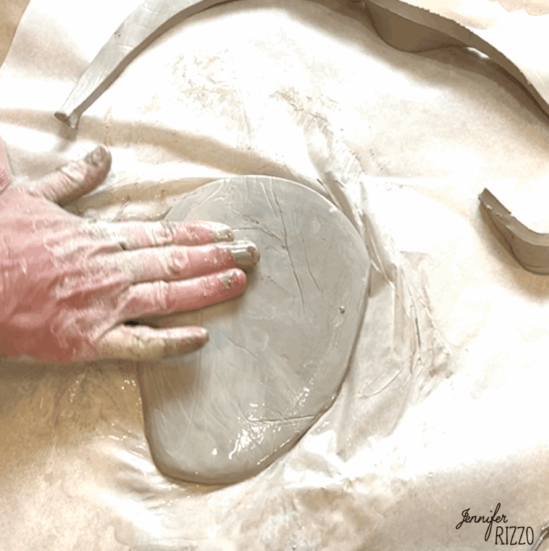 air dry clay strawberry trinket dish 4 a hand smoothing a slab of wet clay on parchment paper, with clay scraps nearby.