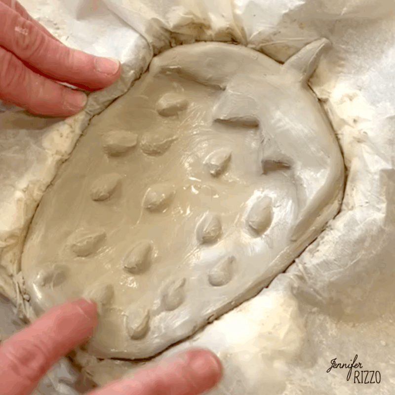air dry clay strawberry trinket dish 10 a person shapes a clay strawberry with textured seeds on a piece of parchment paper.