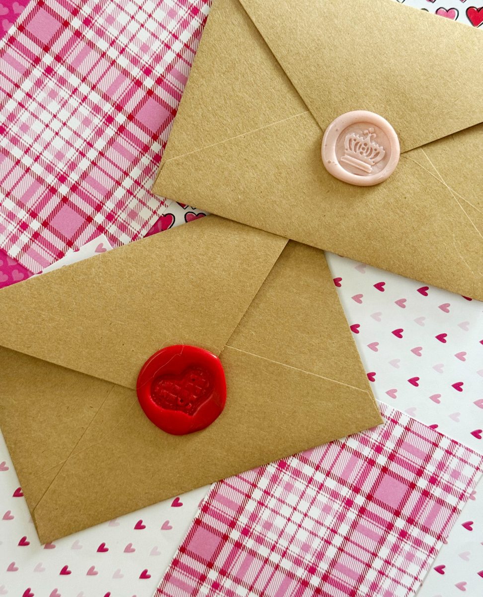 two brown envelopes sealed with red and pink wax stamps, placed on top of pink plaid and heart-patterned paper.
