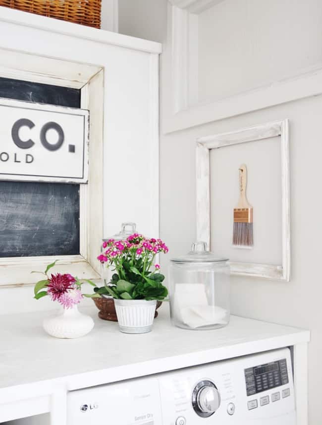 how i wake up my house 12 a neat laundry room corner with a white washing machine, topped with decorative items including a sign, fresh flowers in various containers, and a framed paintbrush to decorate your walls.