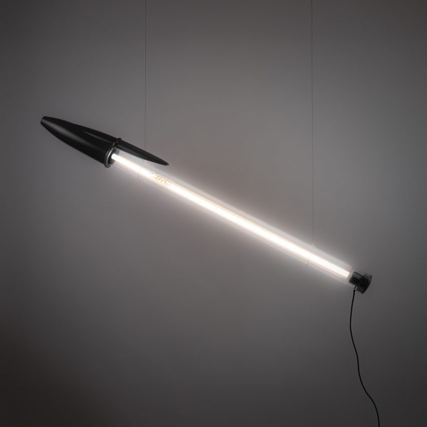 pen-shaped lamp suspended in front of grey backdrop