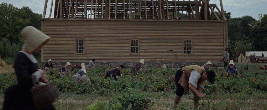 still from the testament of ann lee showing shakers labouring under the shadow of a partially built timber-framed building