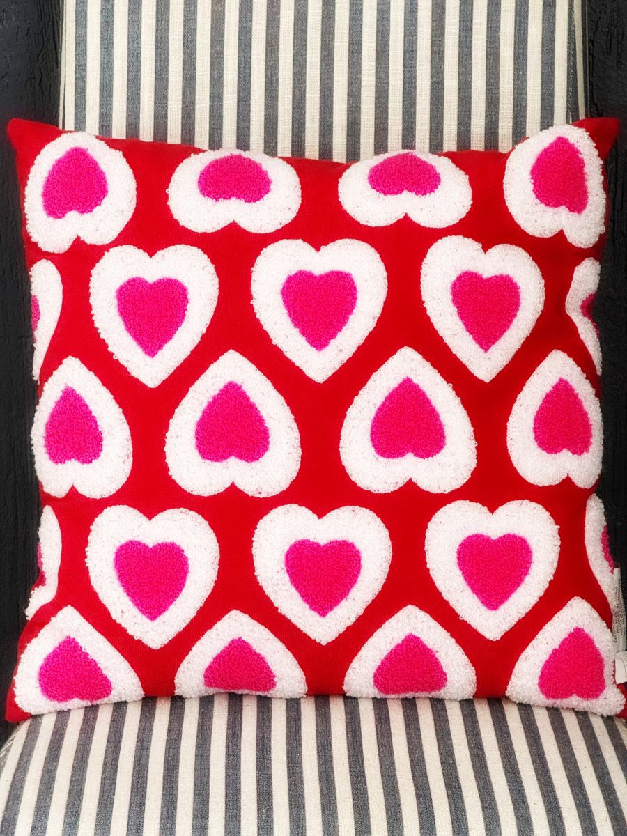 a red pillow with a pattern of white and pink hearts sits on a chair with black and white vertical stripes.