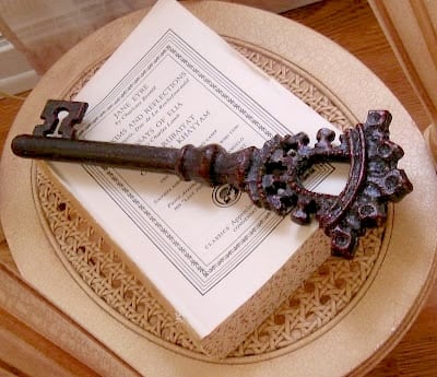 different ways to use vintage books in decorating 2 a large, ornate antique key rests on top of a closed book with a decorative cover—perfect inspiration for the removal of covers from books for decorating—placed elegantly on a woven surface.