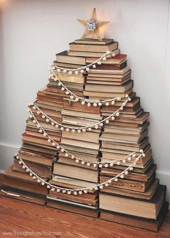 different ways to use vintage books in decorating 11 a stack of books arranged in the shape of a christmas tree, decorated with a light garland and topped with a star.