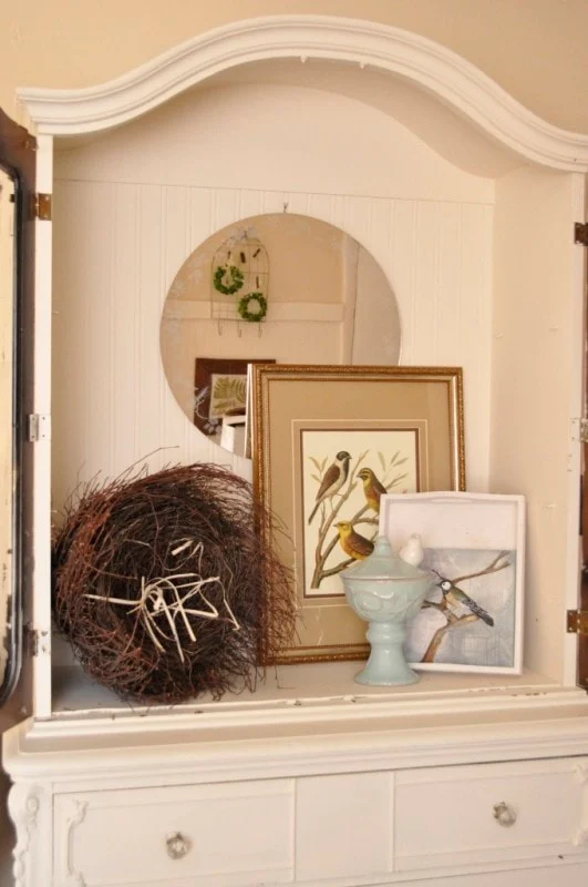 ways to repurpose china cabinets 22 white cabinet with bird-themed framed art, a round mirror, a decorative twig nest, and a ceramic dish holding a small white bird figurine—an inspiring example of furniture makeovers before and after.