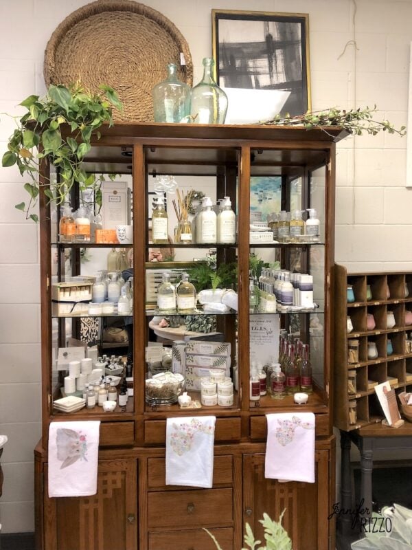 ways to repurpose china cabinets 27 a wooden cabinet displays various bath and body products, decorative jars, towels, and plants, with framed art and baskets on top.