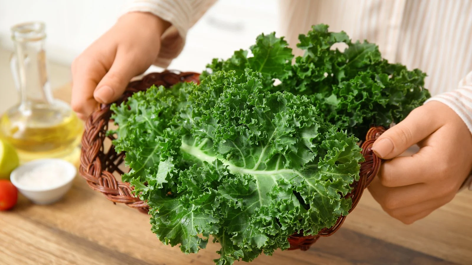 a close-up shot of a person holding a small basket of freshly harvested leafy crops, all situated in a well lit area indoors