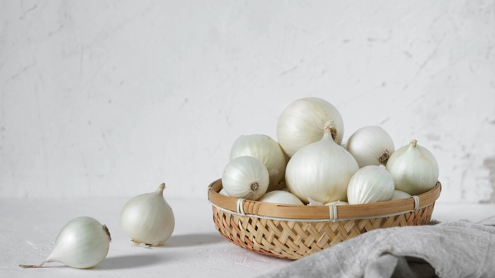 glossy white gladstone allium cepa bulbs piled in a light woven basket, smooth and round.
