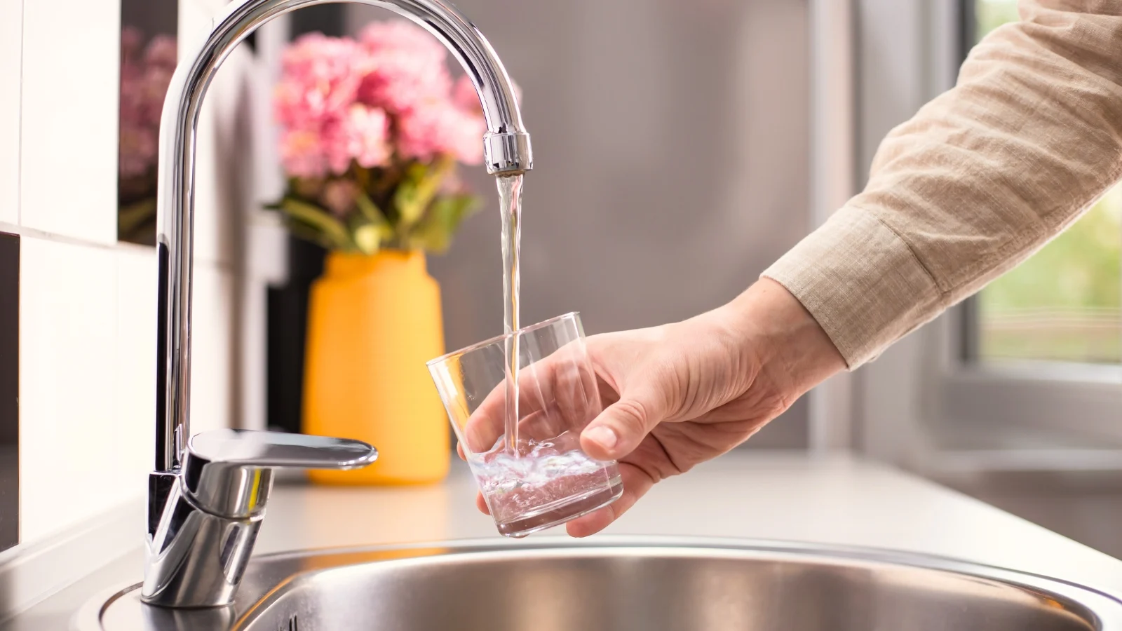 a close-up shot of a person's hand holding a glass, and filling it with liquid from the sink, all situated in a well lit area indoors