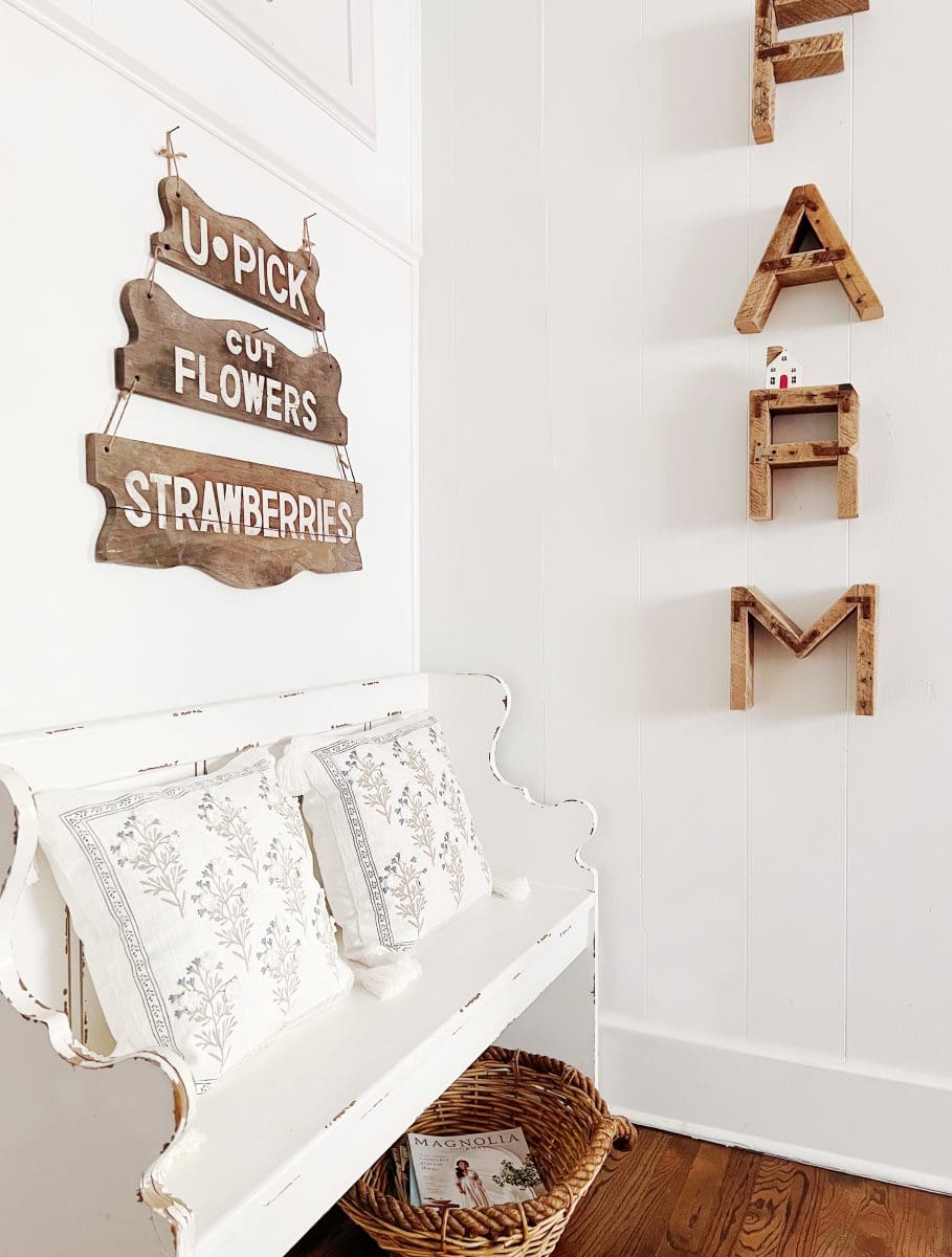 a cozy corner in the spring kitchen decorated with a rustic white bench adorned with floral cushions, a sign for fresh flowers and strawberries, and decorative wooden ladders on a shiplap wall, evoking