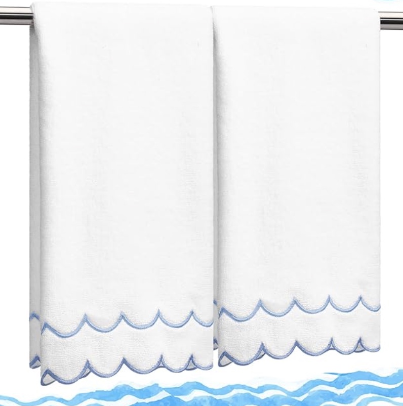 two white towels hang side by side on a silver bar. each towel has a scalloped edge with light blue embroidery, and there are blue wavy lines illustrated at the bottom of the image.
