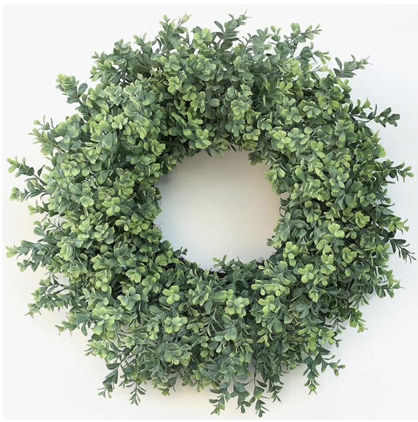a round wreath made of dense green leaves with small light and dark green accents, arranged in a circular shape against a plain white background.
