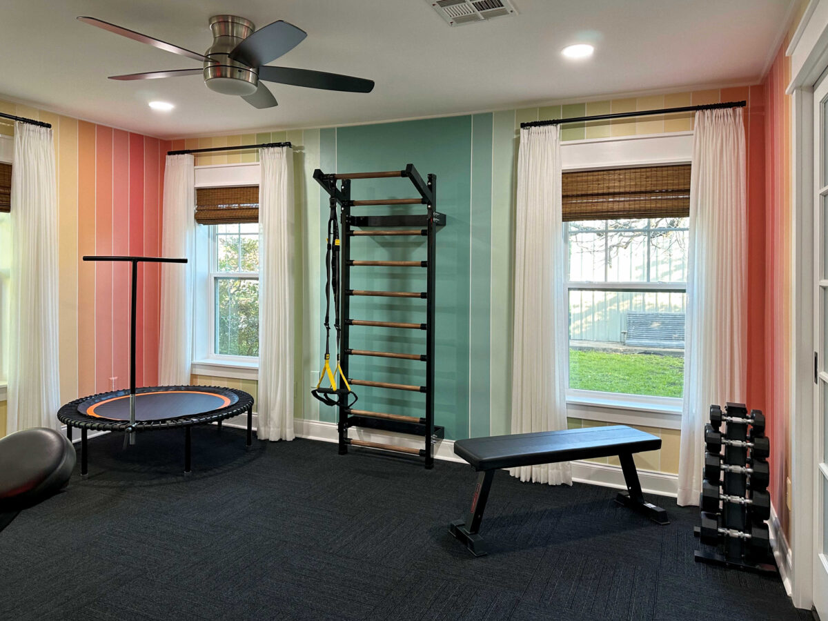 colorful home gym with striped walls, white curtains, and black commercial carpet squares