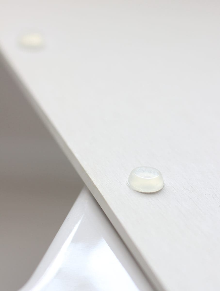 a close-up view of a water droplet resting on a slanted, smooth white kitchen island surface, displaying surface tension and the reflective qualities of water.
