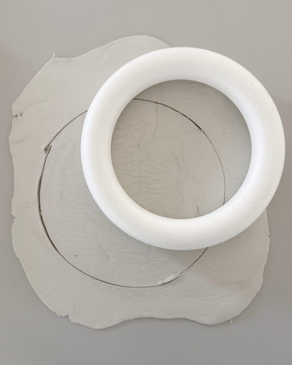 a round white foam ring sits on a sheet of pale clay, with a circle traced in the clay under the ring. the clay has uneven edges and light texture.